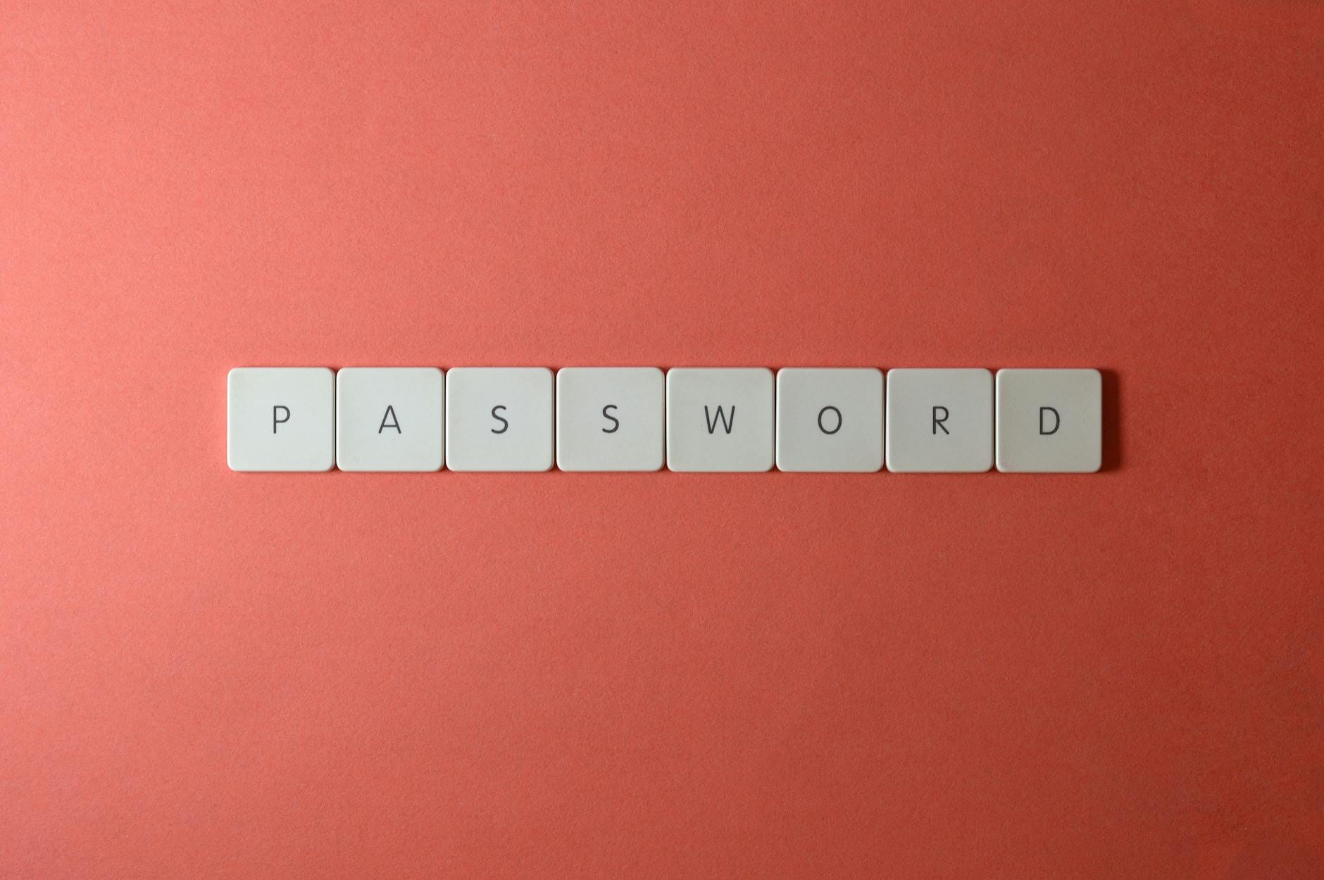 Jak zabezpieczyć konto po wycieku danych: zmiana haseł, 2FA, sprawdzenie sesji Białe klawisze z napisem PASSWORD na koralowym tle, symbol bezpieczeństwa haseł