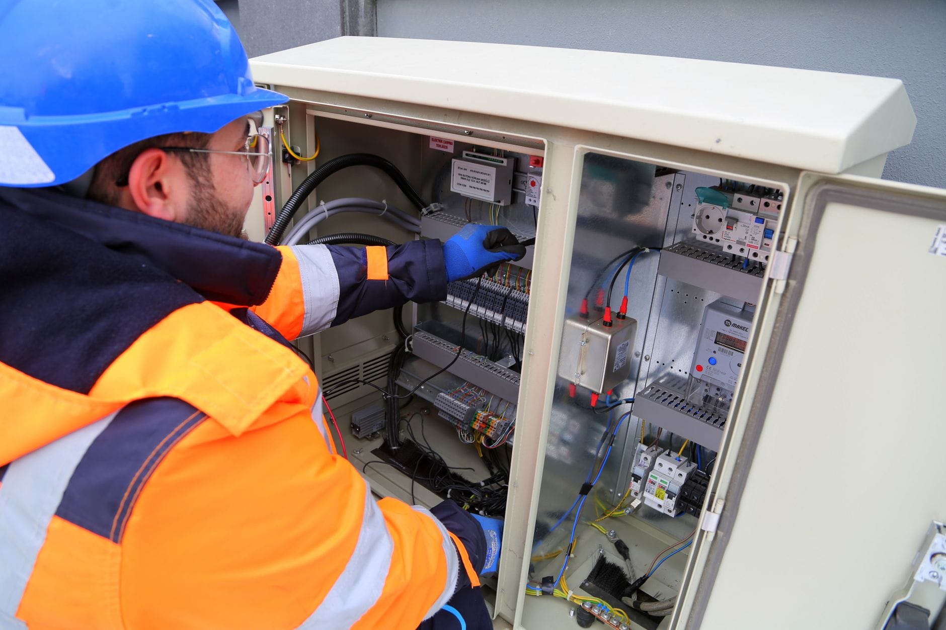 Elektryk w kasku sprawdza zewnętrzną rozdzielnię elektryczną
